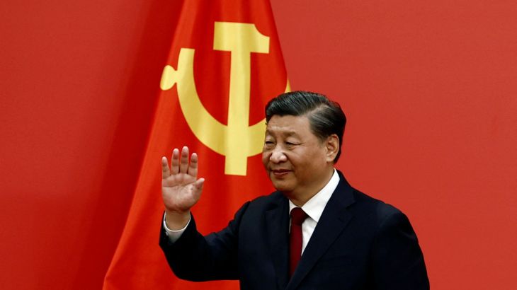 Chinese President Xi Jinping waves as he walks in front of a giant red flag with the hammer and sickle. He looks confident.