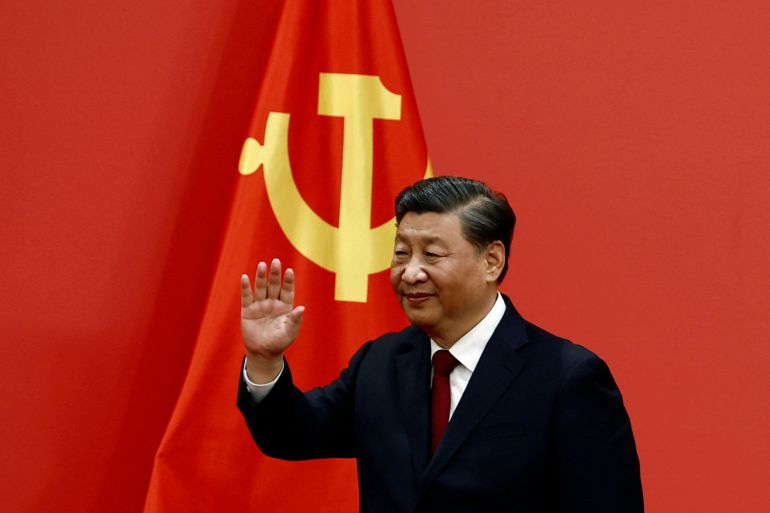 Chinese President Xi Jinping waves as he walks in front of a giant red flag with the hammer and sickle. He looks confident.