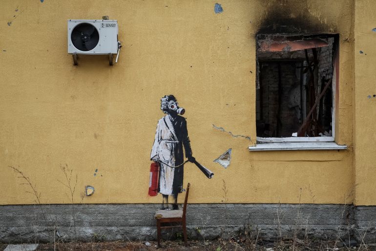 a woman in a gas mask and dressing gown holding a fire extinguisher on the side of a scorched building.