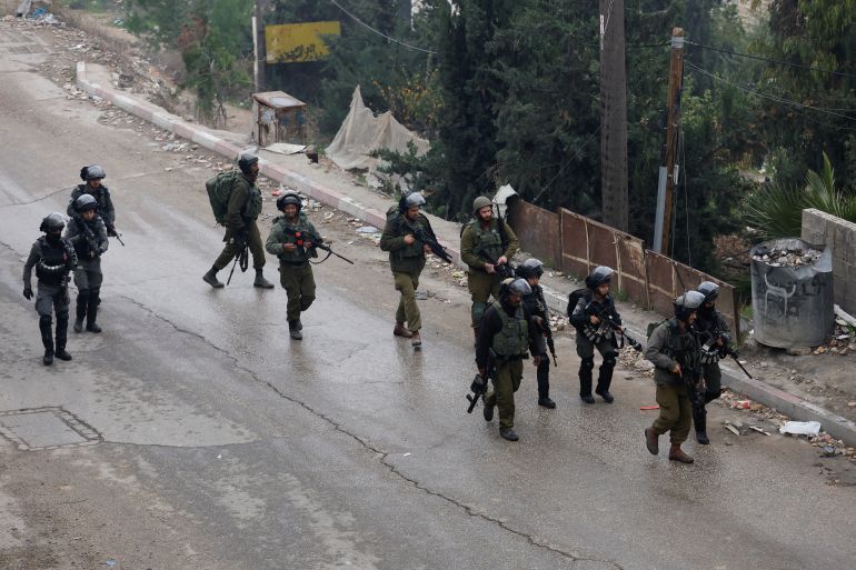 Israeli soldiers walking through a street during a raid in the West Bank