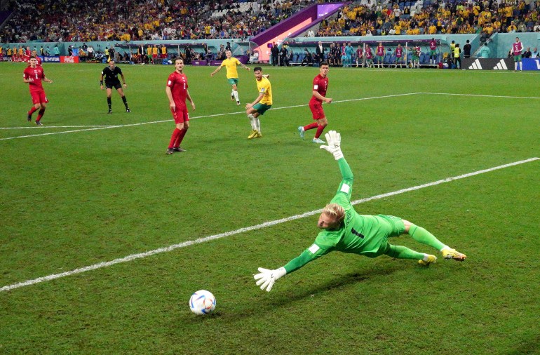Mathew Leckie watches as the ball goes beyond the finger tips of blond-haired Danish goalkeeper and into the net