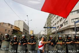 A man waves a Peruvian flag in front of a line of police in Lima