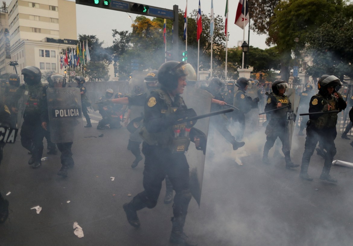 Riot police officers take position among a cloud of tear gas