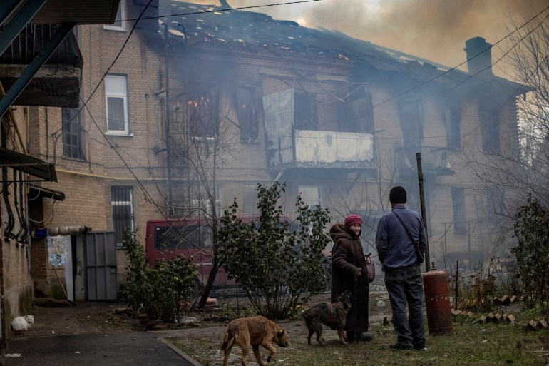 Moradores no quintal de seu prédio destruído observam a fumaça subir em Bakhmut, na Ucrânia.