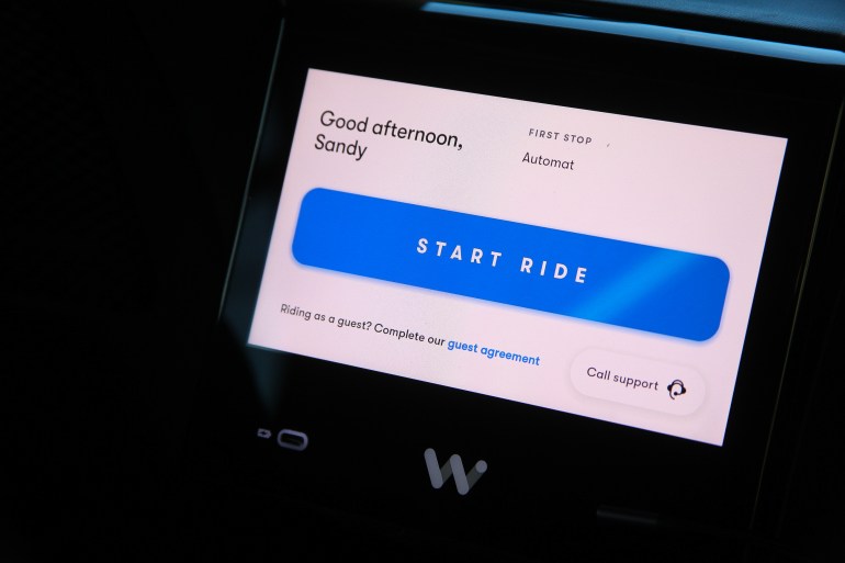 A screen inside a Waymo vehicle, with the text "Good afternoon, Sandy" and a button that reads "Start Ride"