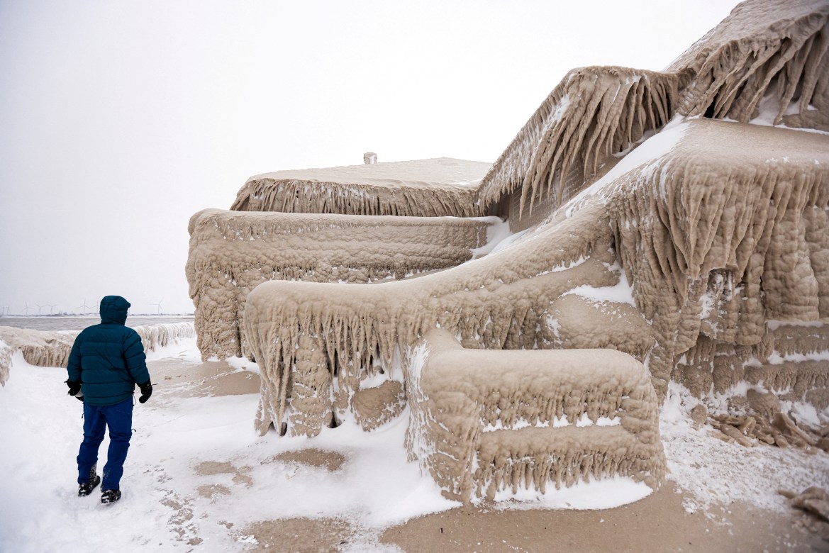 man walks beside ice formed by the spray of Lake Erie waves which covered a restaurant during a winter storm