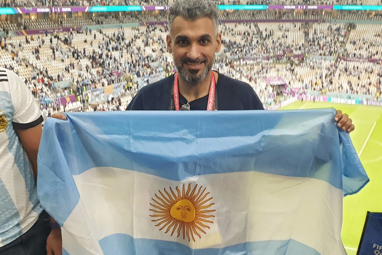 Argentina fan Hani Albashir is holding up the Argentinian flag in the stands and smiling