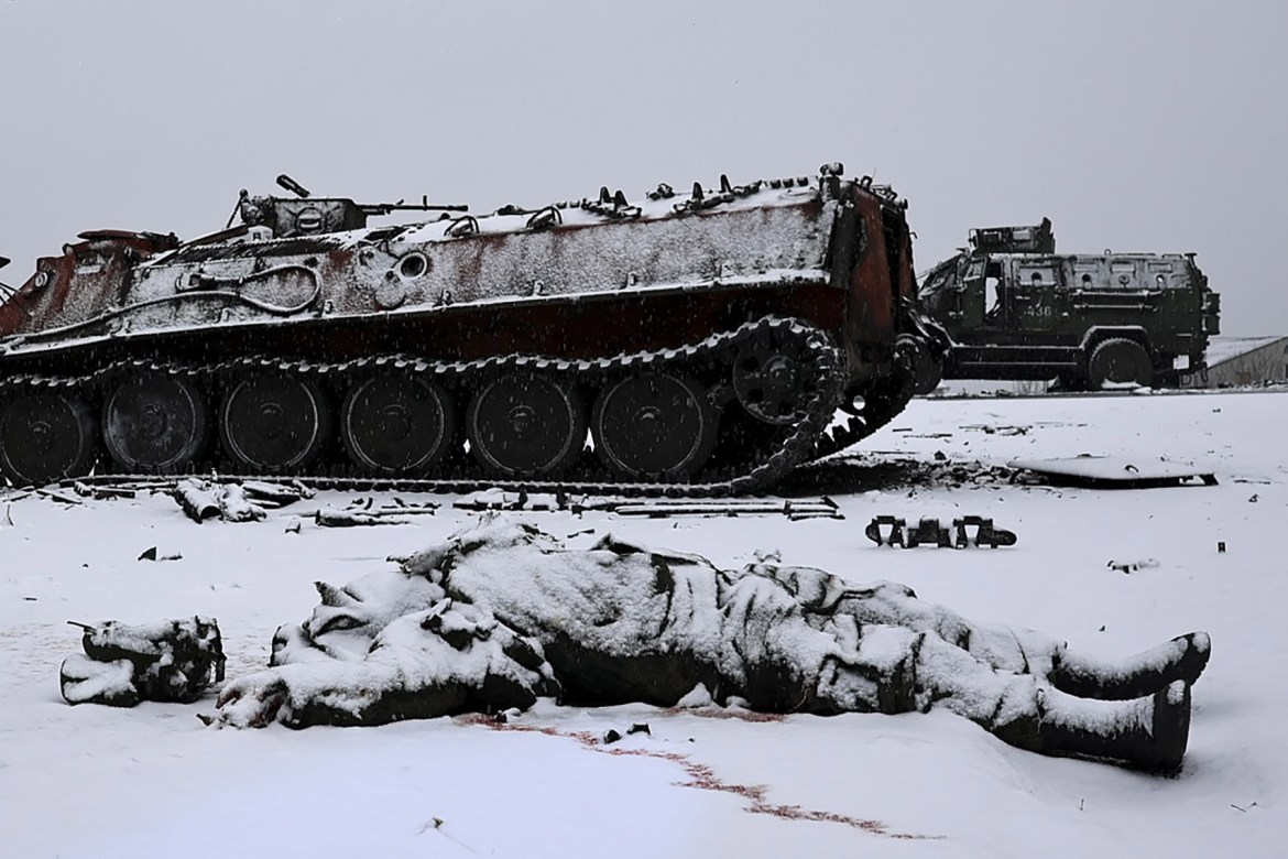 A soldier's lifeless body lies next to a burnt Russian APC