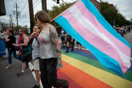 A pair of individuals walk across a rainbow-painted street in Atlanta carrying a transgender pride flag