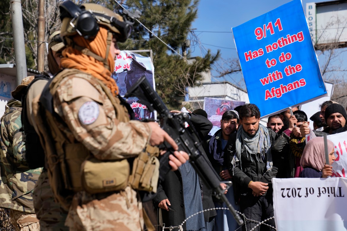 A Taliban fighter stand guards in front of protesters condemning President Joe Biden's decision on frozen Afghan assets in Kabul.