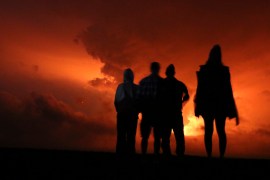 People stand watching the glow of lava erupting from Hawaii&#39;s Mauna Loa volcano, on November 28, 2022, in Hilo, Hawaii. [Caleb Jones/AP Photo]