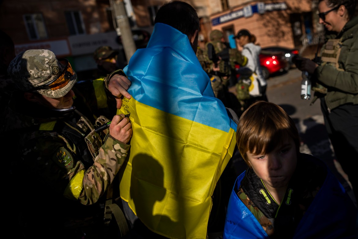 A Ukrainian defense force member signs a Ukrainian flag for a resident in Kherson, southern Ukraine, Monday, Nov. 14, 2022. (AP Photo/Bernat Armangue)