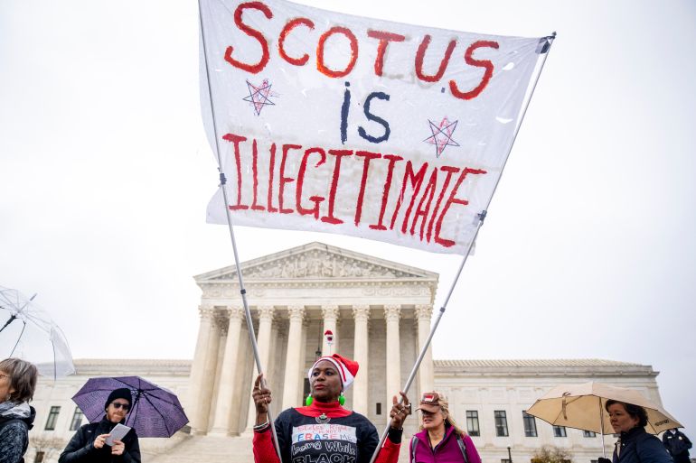 A protester holds a sign that reads "SCOTUS is illegitimate" in front of the US Supreme Court