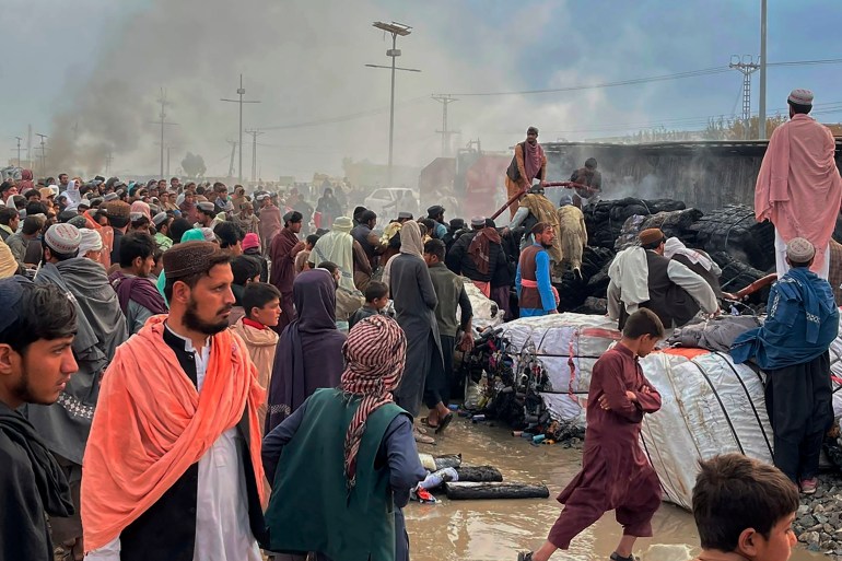 İnsanlar, Afgan güçlerinin Çaman'ı bombalaması sonucu yanmış bir kamyonun yanında toplanıyor.