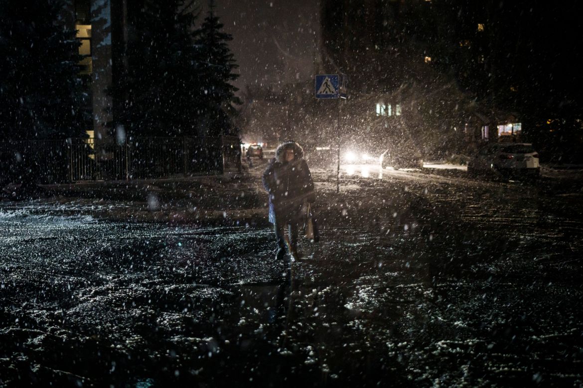 A woman crosses the street during snowfall