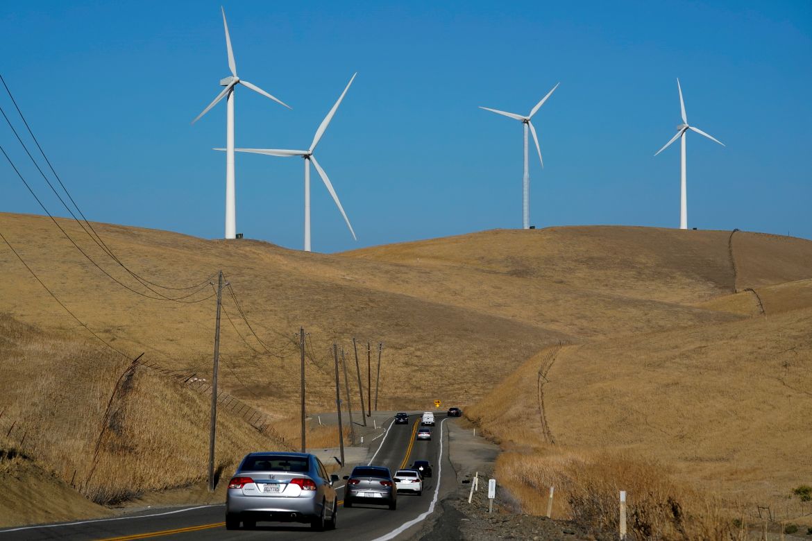 Vehicles move down Altamont Pass Road with wind turbines in the background