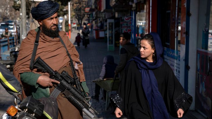 A Taliban fighter stands guard as a woman walks past in Kabul, Afghanistan.