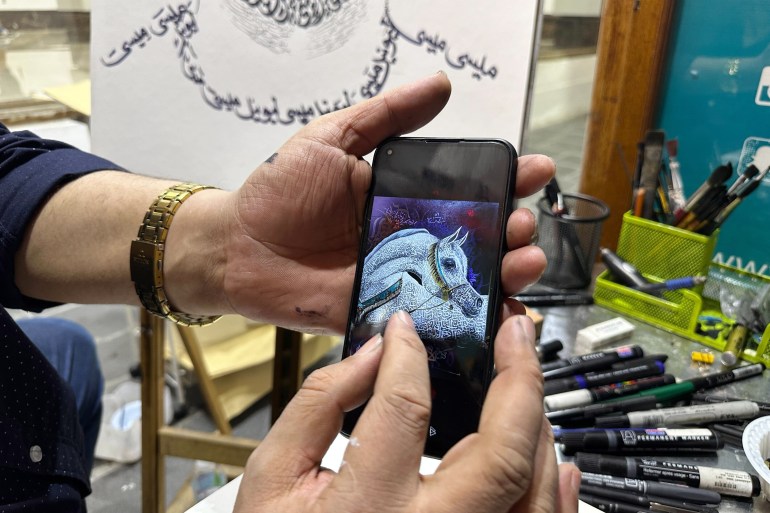 Khaled Almesawy's hands holding an iPhone with a picture of a white horse on it. The easel showing the bottom part Messi's sketch is behind his hands Paintbrushes and pencils lie next to it. He is wearing a gold-plated watch..
