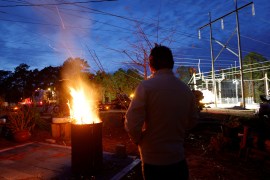 A man stands next to a fire as he watches repair work