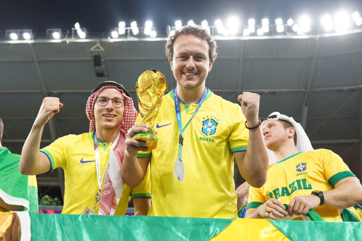Brazil fans cheering in the stands prior to the start of the match. One of them is holding a replica of the golden World Cup trophy.