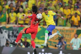 Rapinha in mid-air, trying to head the ball with a South Korea defender tackling him.