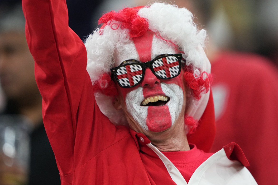 An England fan celebrates, his face painted in the team's white and red colours.