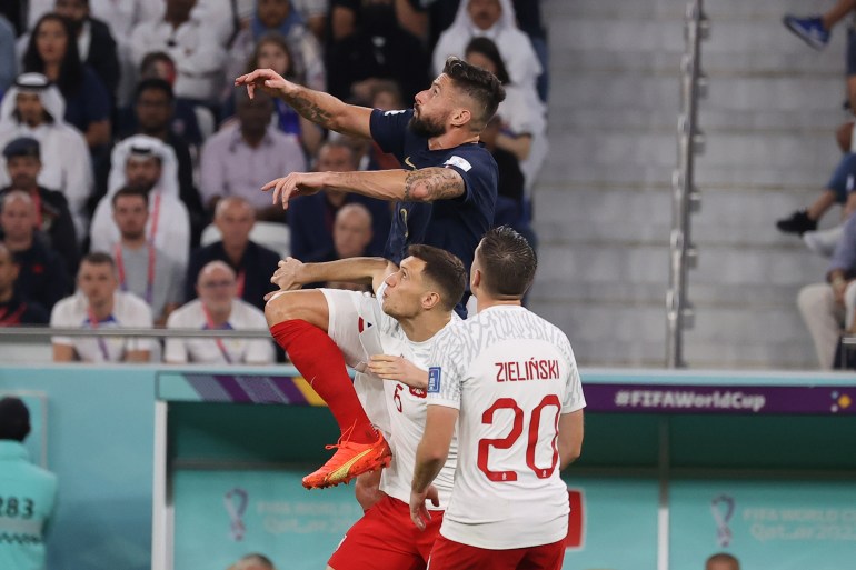 France’s Olivier Giroud jumps above two Polish defenders and heads the ball.