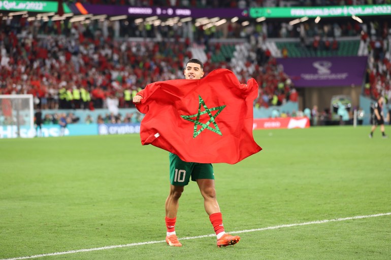Morocco's Anass Zaroury walks on the pitch with a Moroccan flag.