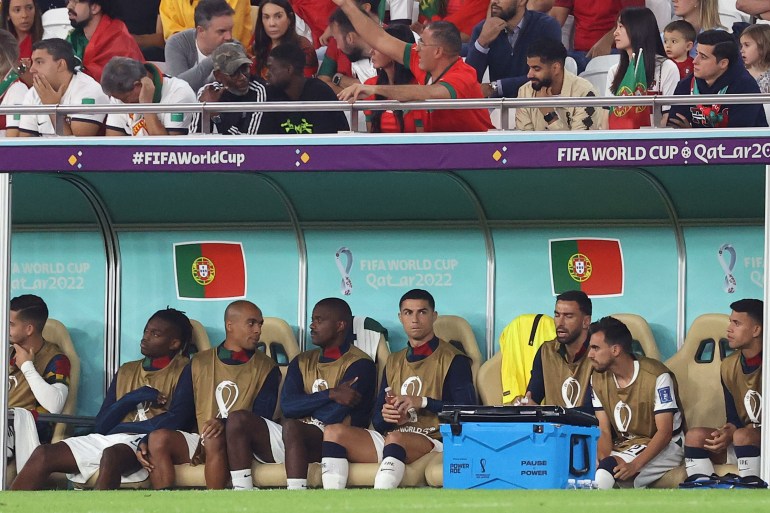 Ronaldo zit op de bank geconcentreerd naar de wedstrijd te kijken terwijl de andere spelers naast hem met elkaar praten