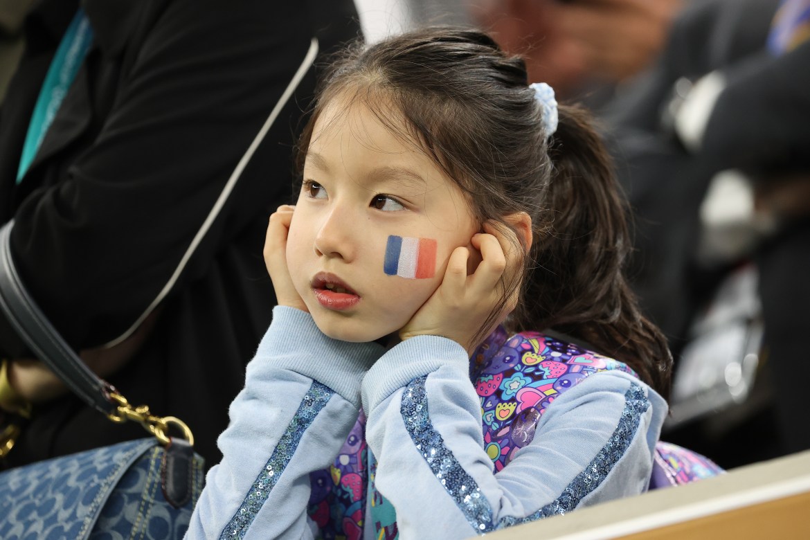 A young girl, with the French flag painted on her cheek, looks on from the stands.
