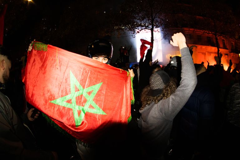 Masked person waves a Moroccan flag during night-time celebrations