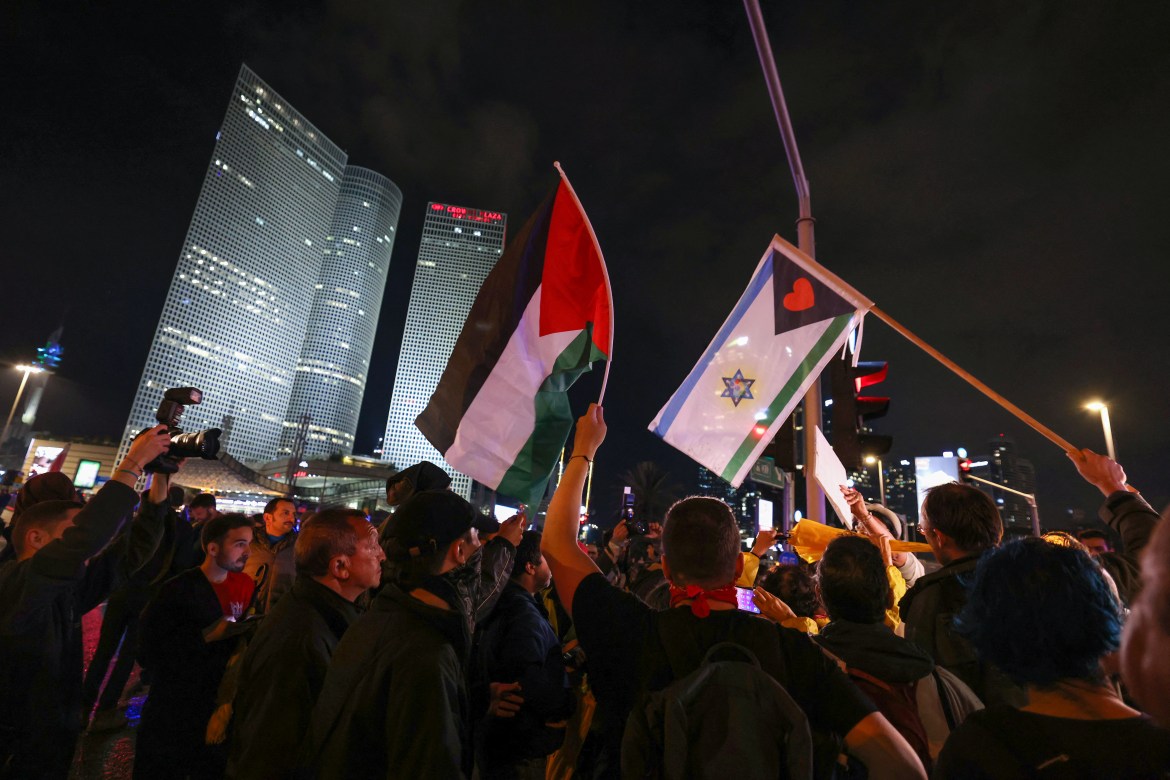 Protestatari israelieni ridică un steag palestinian în timpul unui miting împotriva noului guvern de dreapta dură al premierului Benjamin Netanyahu. [Ahmad Gharabli/AFP]