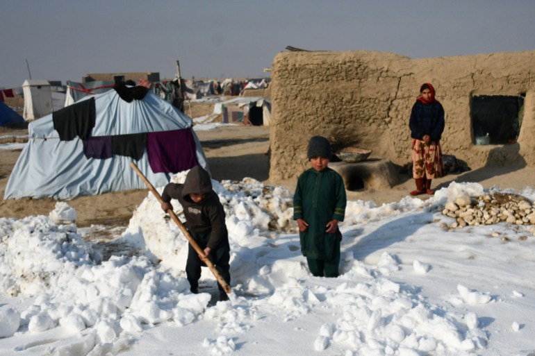 Crianças deslocadas internamente afegãs removem a neve perto de suas barracas durante um dia frio de inverno no distrito de Nahr-e Shah-e-, na província de Balkh