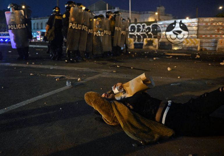 A demonstrator affected by tear gas shot by riot police lies in the street during a protest demanding the resignation of Peru's President Dina Boluarte in Lima on January 23, 2023. - Civil unrest since the ouster of Dina Boluarte's predecessor, Pedro Castillo, in early December has left 46 people dead and prompted the government to impose a state of emergency in violence-hit areas.