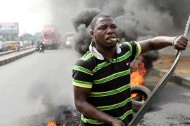A protester walks past burning tyres with a lighter held in his teeth during a rally against fuel price hikes in Lagos, Nigeria, on January 3, 2012. These tools, common sights in protests, are also weapons used in lynchings in Nigeria [Akintunde Akinleye/Reuters]
