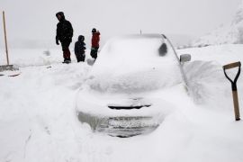 People stand near a car which got stranded during a snowstorm near Barrios de Luna, in northern Spain, February 5, 2015. REUTERS/Eloy Alonso (SPAIN - Tags: ENVIRONMENT SOCIETY)