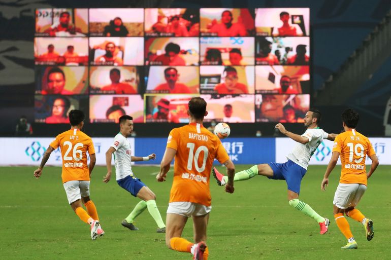 Soccer Football - Chinese Super League - Wuhan Zall vs Qingdao Huanghai - Suzhou, Jiangsu province, China - July 25, 2020. Players of Wuhan Zall in action against players of Qingdao Huanghai in front of a giant screen showing fans watching the match online, as it resumes following the coronavirus disease (COVID-19) outbreak. cnsphoto via REUTERS. ATTENTION EDITORS - THIS IMAGE WAS PROVIDED BY A THIRD PARTY. CHINA OUT.
