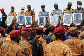 Burkina Faso soldiers hold portraits as they stand in front of the coffins of 27 soldiers killed in an attack by armed fighters in the north of the country in October, 2022 [File: Vincent Bado/Reuters]