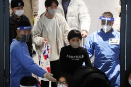A Chinese woman walks out of Seoul airport accompanied by a soldier in a blue hazmat suit
