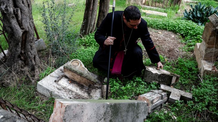Archbishop Hosam Naoum inspects a vandalized tombstone at the Protestant Mount Zion Cemetery