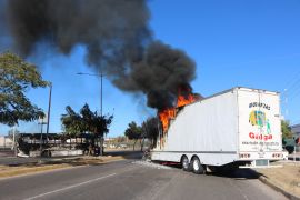 The burnt wreckage of a bus and a burning truck