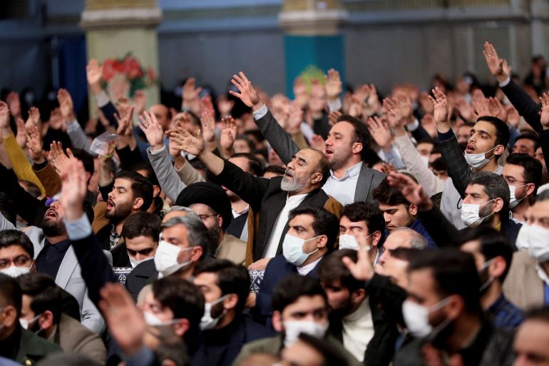 Iranian government supporters raise their hands in a crowd in a hall