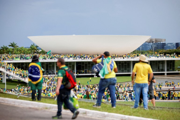 Demonstrators wearing green and yellow shirts are seen atop government buildings in Brasilia, as well as on the lawn below. Some are draped with the Brazillian flag.