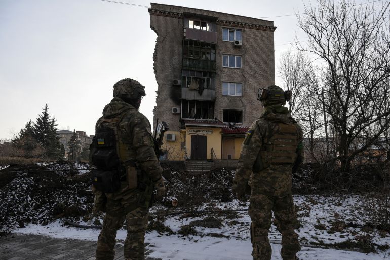 Ukrainian servicemen stand next to a damaged residential building in Bakhmut