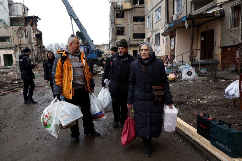 Pessoas ficam entre os destroços de um prédio de apartamentos danificado pelo bombardeio russo no Dnipro da Ucrânia