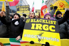 Protesters wave flags and hold placards, one of which says 'Blacklist IRGC'