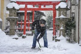 A man shovelling snow in front of a red shrine gate in Japan's Tottori