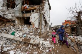 A woman and two children walk next to a house damaged by a Russian military strike in Hlevakha, outside Ukraine&#39;s capital, Kyiv [Valentyn Ogirenko/Reuters]