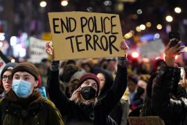 A person holds a sign during a protest following the release of videos showing Memphis police officers beating Tyre Nichols. 'End Police Terror' is written in big letters on the sign that is held overhead.