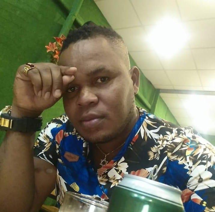 Christopher Osinanna Nwadik wears a floral shirt and holds his hand to his forehead.